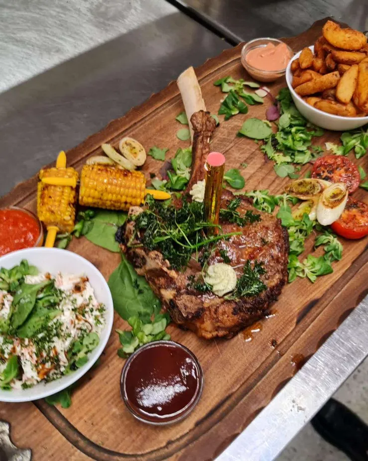 Grillplatte mit Steak, Maiskolben und Beilagen auf dem Holzbrett